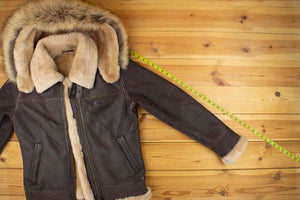 Brown shearling jacket with a fur-lined hood, placed on a wooden surface.
