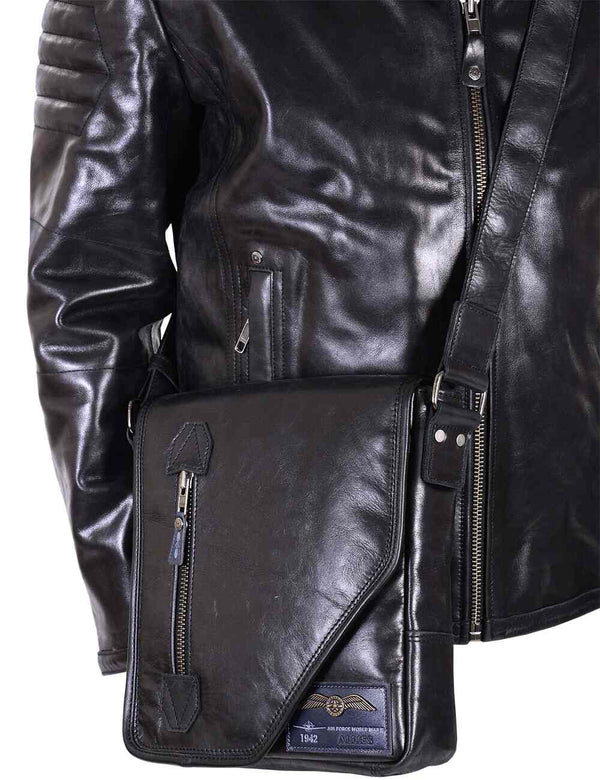 A men's black leather bag is worn over the shoulder of a black leather jacket.