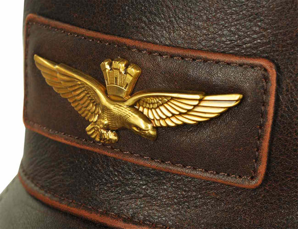 A metal emblem in the form of an eagle with a golden crown on the forehead of a brown leather men's cap.