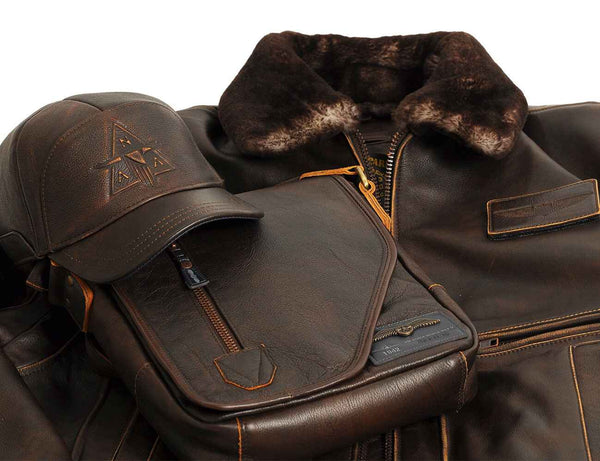 Brown men's leather cap and bag are placed on top of men's leather jacket with fur collar.
