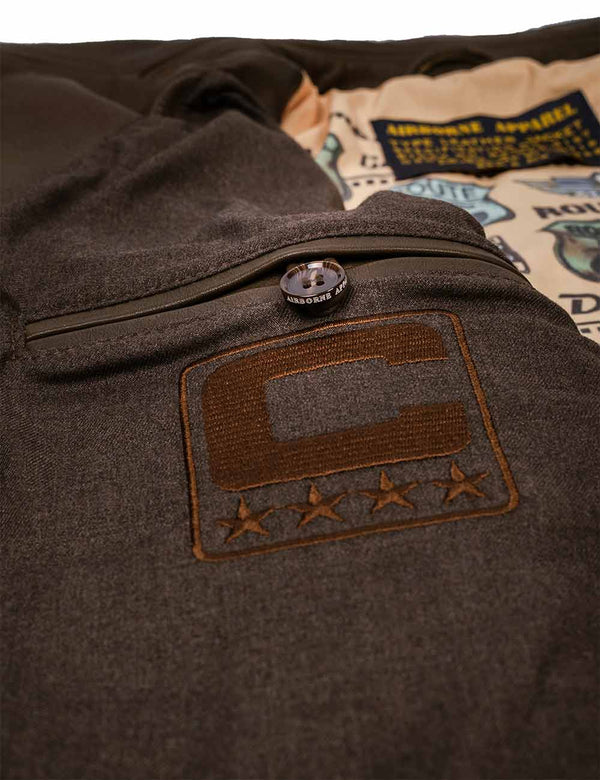 Internal button pocket of a brown jacket with a logo and brand name on a textured background.