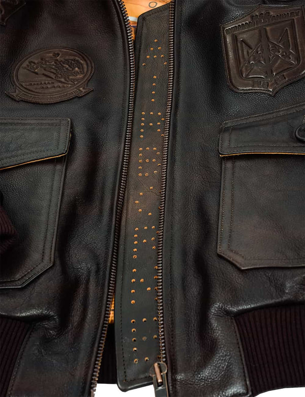 Part of a men's brown leather jacket with patches, unzipped.