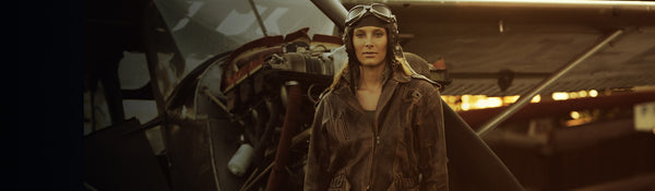 A women wearing vintage aviator gear, including a worn leather jacket and pilot goggles, stands in front of an old aircraft at sunset. The scene has a nostalgic, historical ambiance with warm, golden lighting.