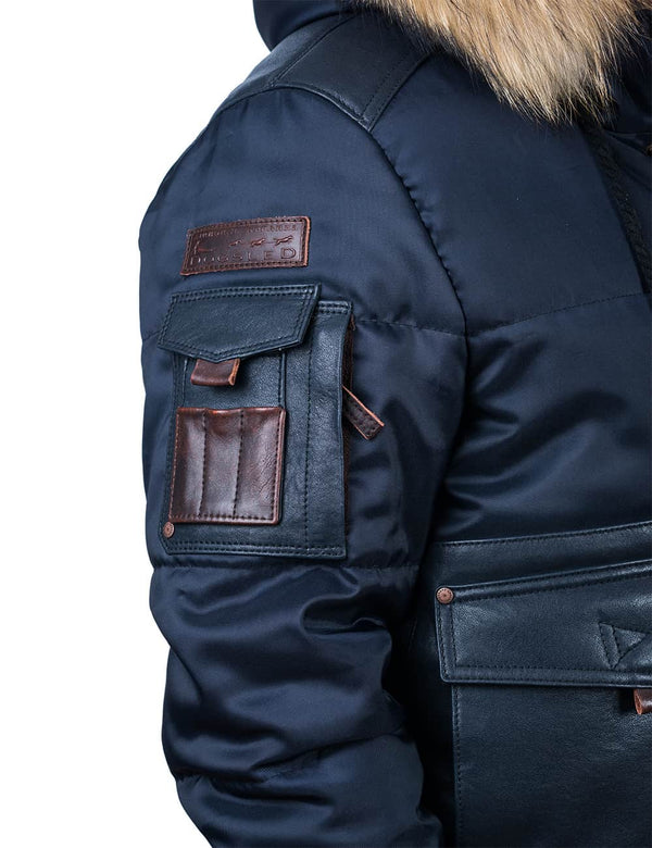 Utility pocket and leather patch on the sleeve of a men's dark blue jacket with a raccoon fur trimmed hood.