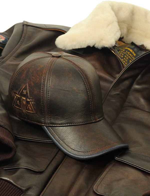 Men's brown leather cap with side embossing placed on short leather brown jacket with cream collar.