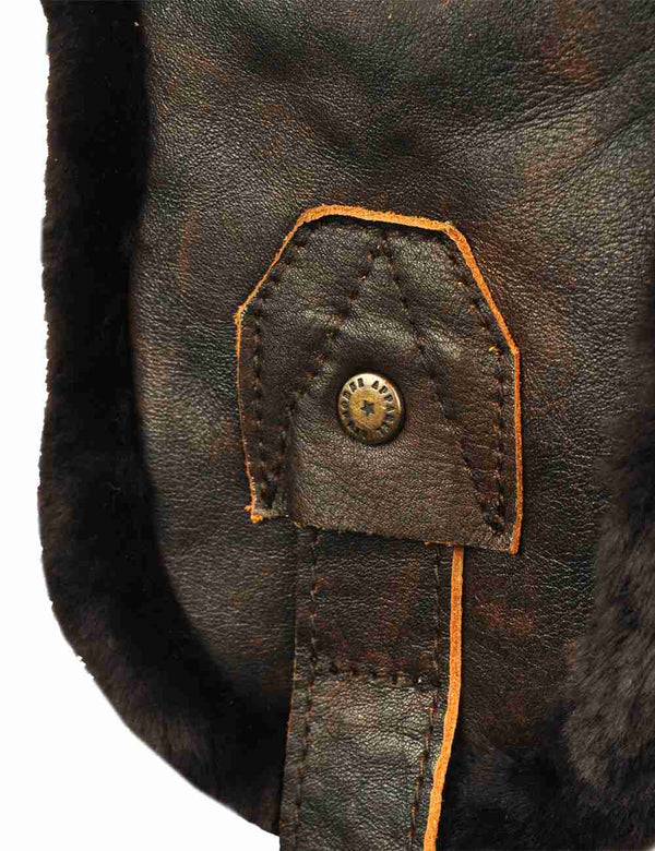 Leather detail with metal button on the ear flap of a sheepskin hat