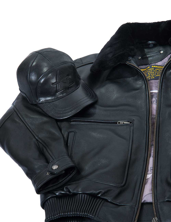 A black embossed men's cap is placed on top of a black leather men's jacket with a fur collar.