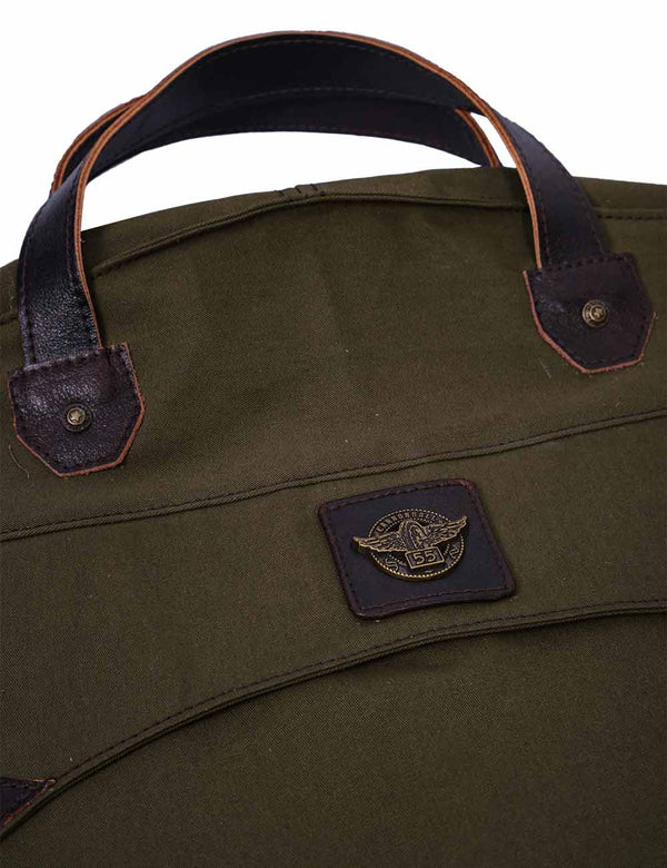 Close-up of the dark brown leather handle and logo patch on the olive green garment bag.