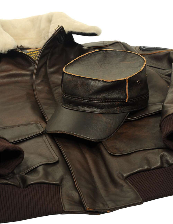 Men's brown leather flat top cap  over a brown leather jacket with elasticated waistband, pockets and cream shearling collar.