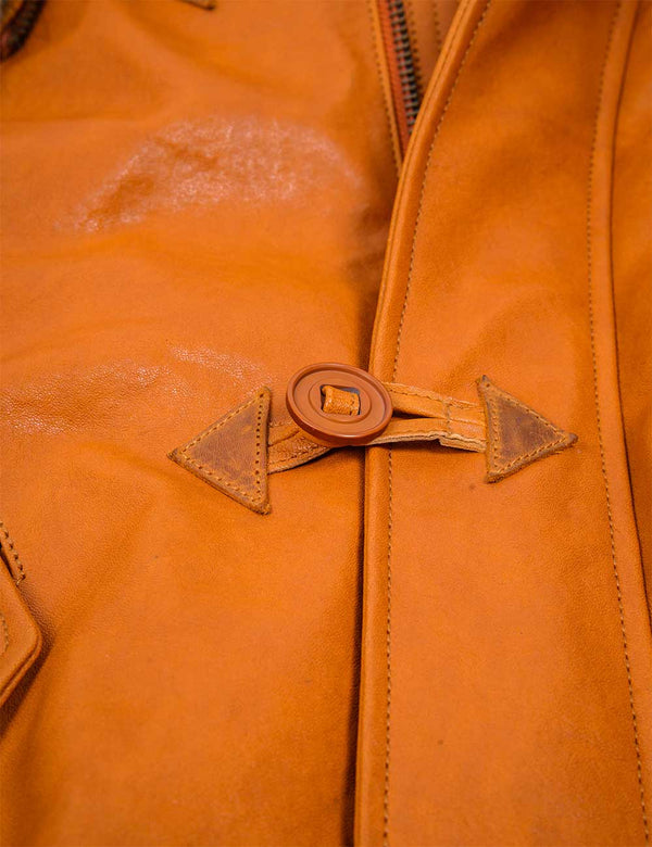 A fastened button of a men's orange leather jacket.