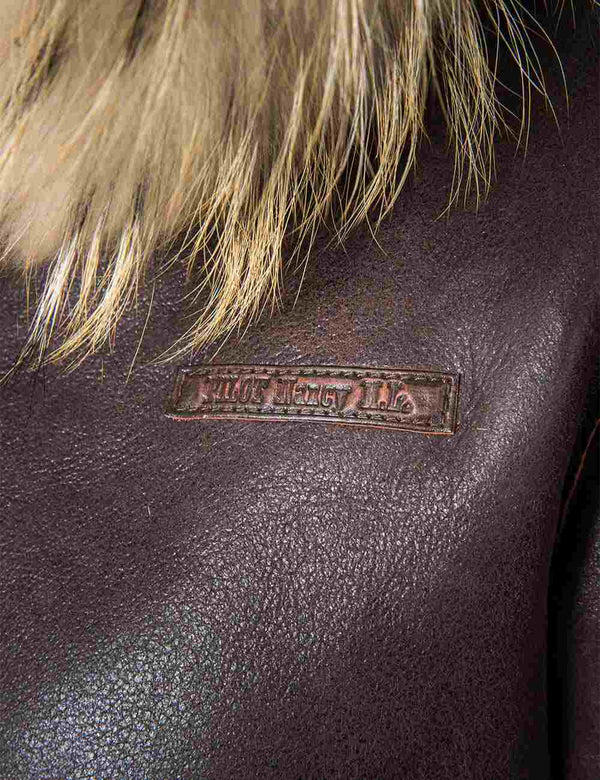 Name tag on the chest of a women's short brown sheepskin coat with a hood.